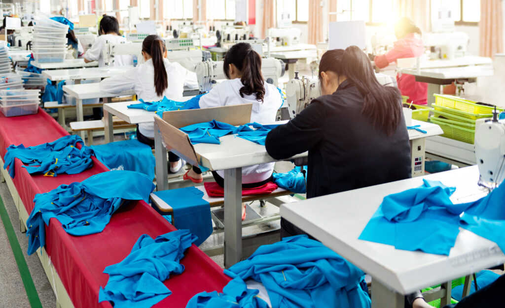 Rear view of female workers working at sewing machines in clothing factory in a row